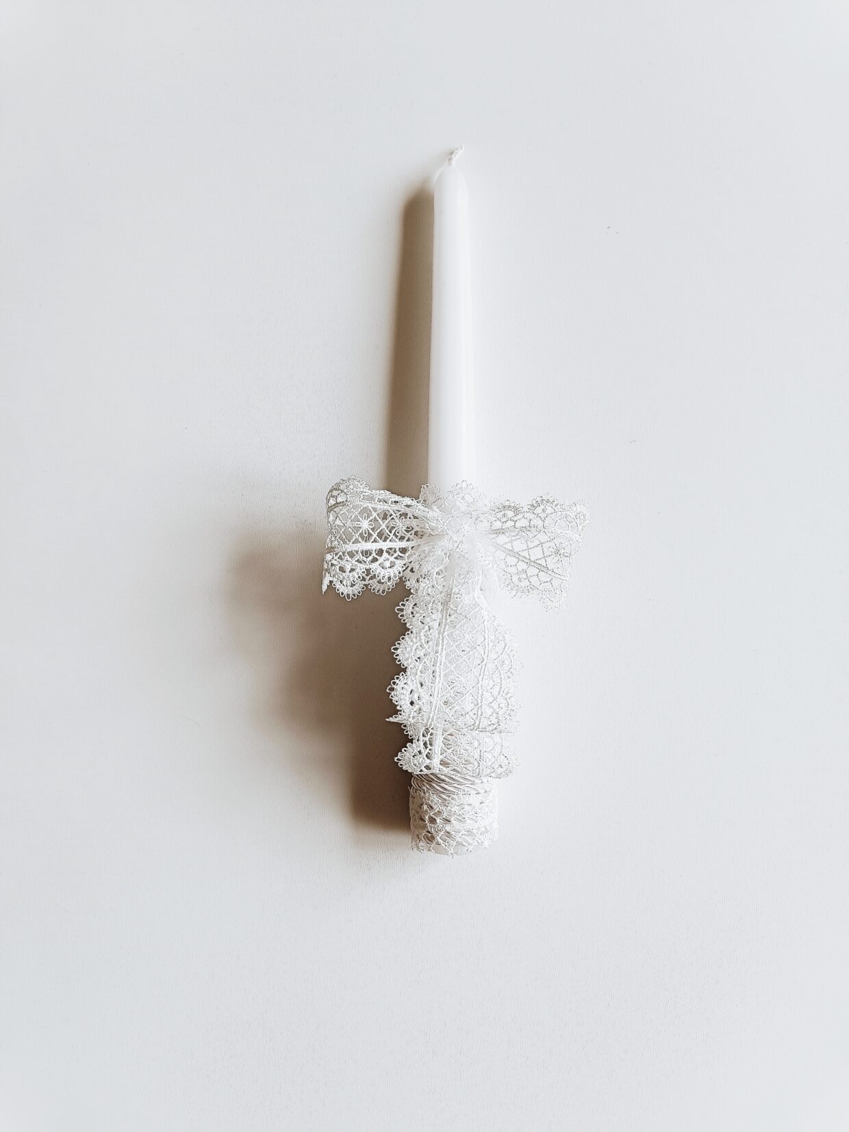 Balta krikštynų komunijos žvakė, dekoruota baltu kaspinėliu.